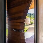 Morpheus Door swung open on its pivot, stacked wood blocks fanning into a spiral, with a garden and stone steps beyond. Project 035 by Whitebird Woodcraft