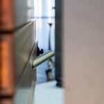 Brushed steel lever handle on the Morpheus Door in soft focus against the stacked wood blocks. Project 035 by Whitebird Woodcraft
